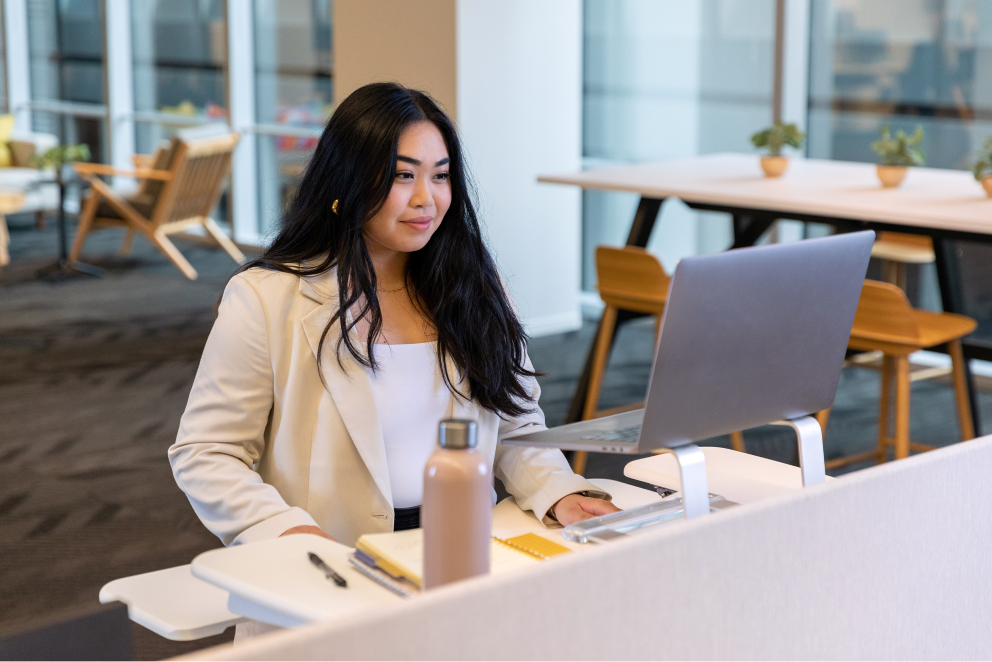 A raven-haired, female-identifying Sprout employee stands at her desk as she works on her laptop